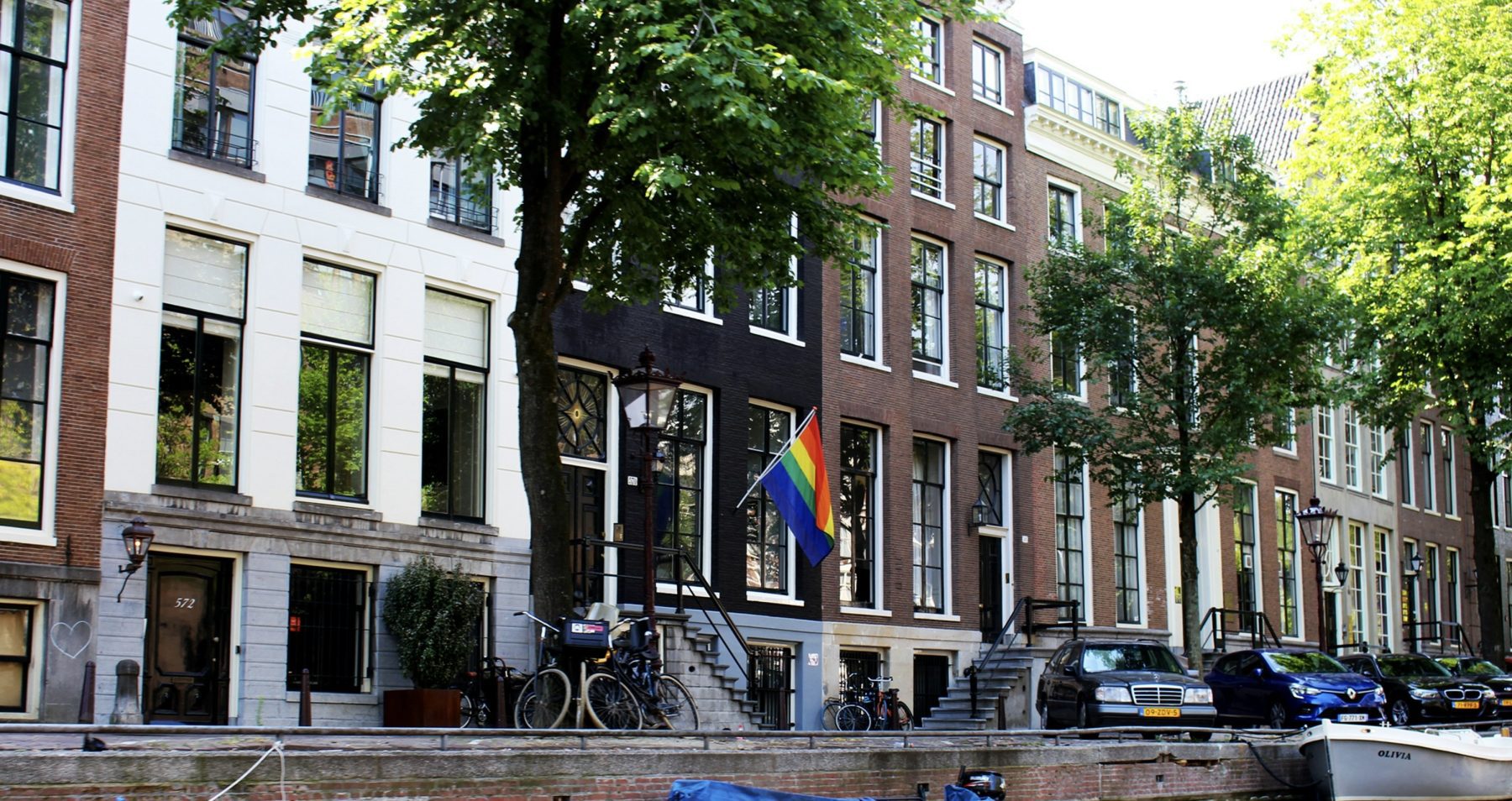 Amsterdamse grachtenpanden met een regenboogvlag aan de gevel.