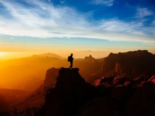 Een persoon op een gebergte tijdens een hike op Gran Canaria met de zonsondergang op de achtergrond.